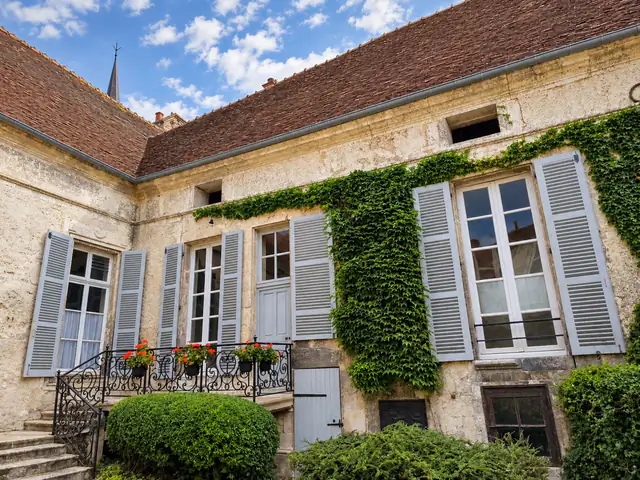La façade au balcon : la vigne vierge dessine ses lignes entre les fenêtres